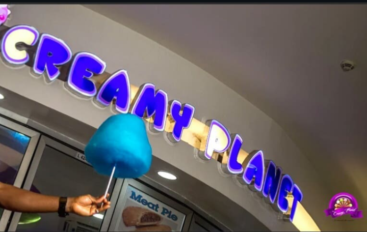 Blue candy floss held up under the glowing Creamy Planet shop sign